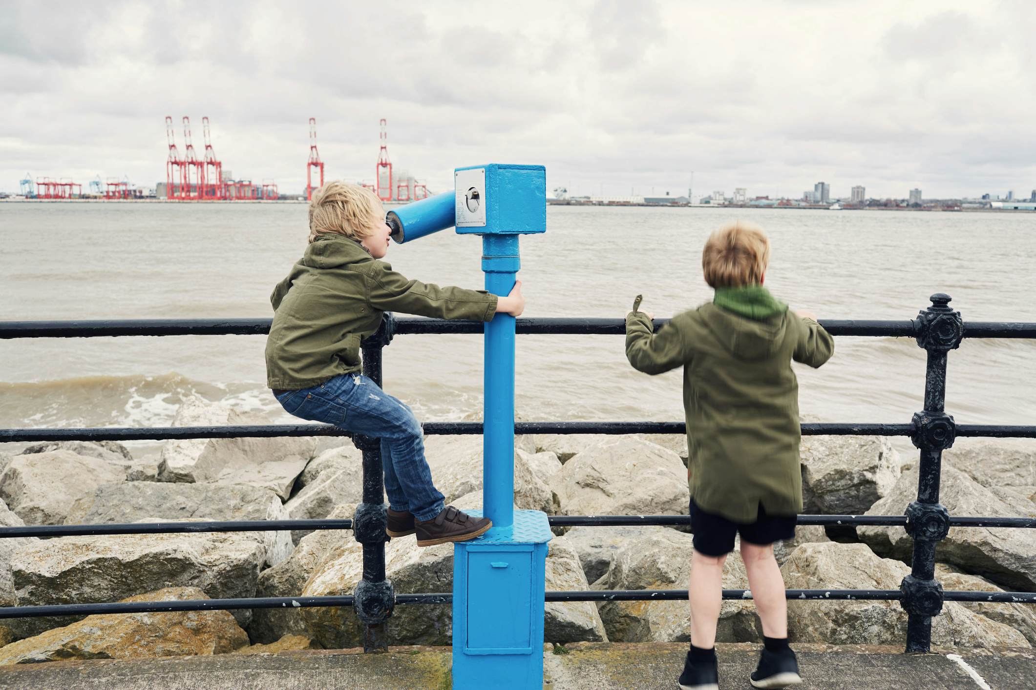 Two little boys using a telescope to look at the view of Liverpool across the The river Mersey from New Brighton